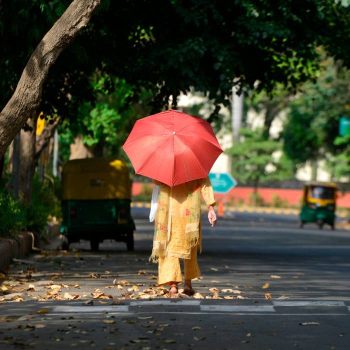 Sarı sari giymiş bir kadın kırmızı bir güneş şemsiyesiyle kendini güneşten koruyor.