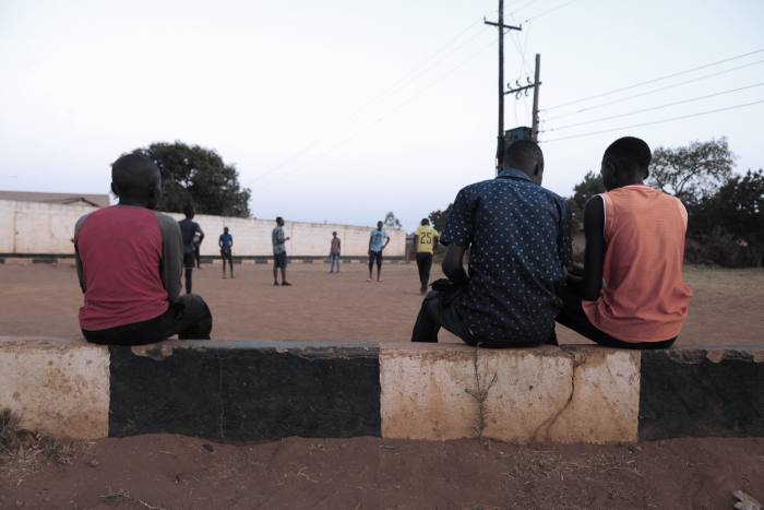 Three people sat down in Kabwe, watching others in the distance  