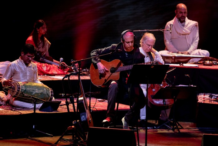A man plays acoustic guitar with an ensemble of musicians on stage