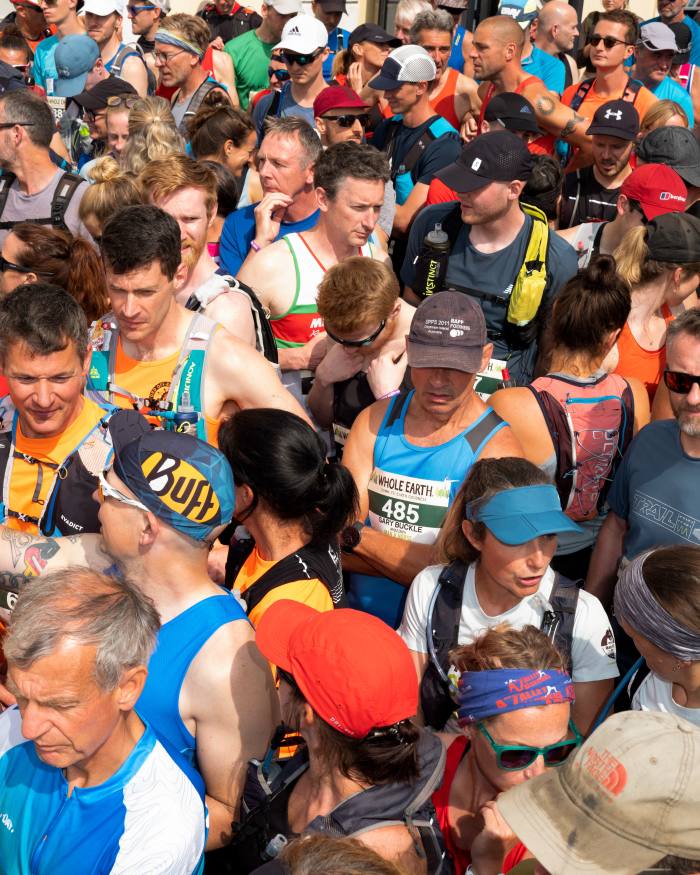 A crowd of runners seen from above, gathering for the race in the sunshine. They are all wearing their race numbers and running gear 