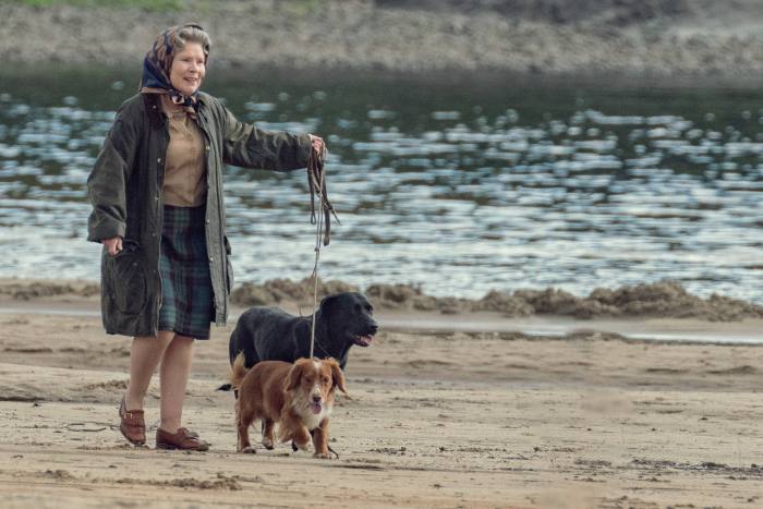 Una mujer con impermeable y pañuelo en la cabeza pasea a dos perros por la playa