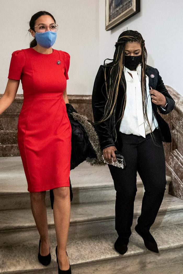 Alexandria Ocasio-Cortez in a red dress and Cori Bush in a black blazer descending a staircase at the US Congress
