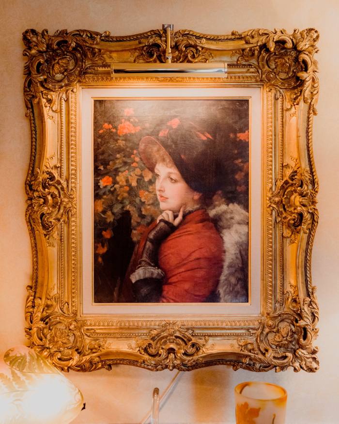A portrait of a woman in red coat and black hat, in an ornate gilt frame