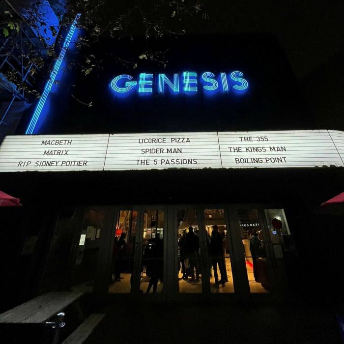 The exterior of the Genesis cinema at night, with its blue neon sign