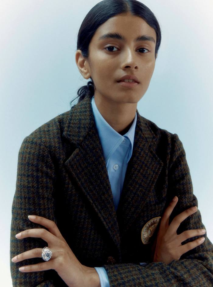 A young woman wearing a coat and shirt and a large ring on her right ring finger