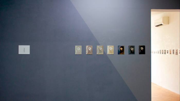 Una exhibición de galería con varias obras de arte pequeñas colgadas en fila, que parecen mostrar variaciones de una imagen de Cristo.