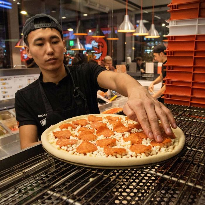 An employee adds pepperoni topping to a pizza ahead of cooking inside a Dodo Pizza restaurant