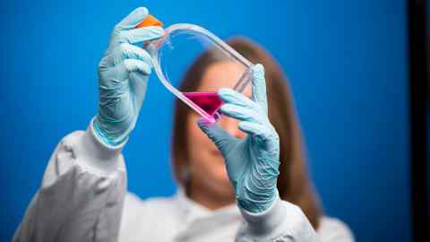 Een vrouwelijke wetenschapper, die blauwe chirurgische handschoenen draagt, houdt een fles paarse vloeistof omhoog in een laboratorium in Cardiff