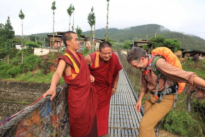 Two monks in red robes laugh with a backpacker