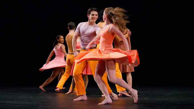 Male dancers in orange trousers and female dancers in orange dresses