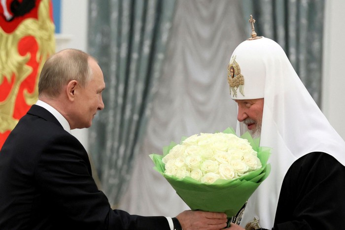 Vladimir Putin presents flowers to Patriarch Kirill at a ceremony last year