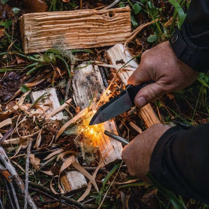 Iemand houdt een mes tegen een stapeltje hout dat vlam vat