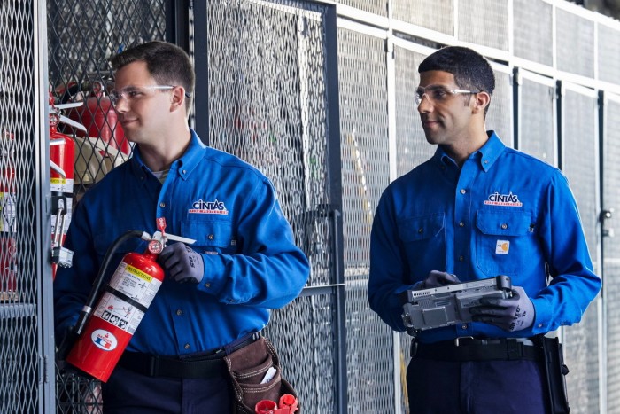 Employees wearing blue-coloured Cintas uniforms. One employee is holding a small fire extinguisher