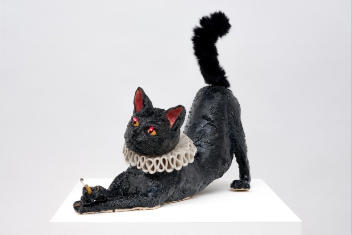 Seekor kucing seramik hitam menghulurkan kaki hadapannya, dengan sebatang rokok di sebelah kaki