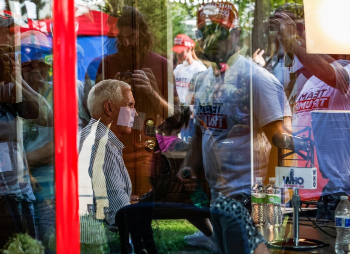 People wearing Trump T-shirts are seen reflected in a window. Through the glass a man can be seen sitting down