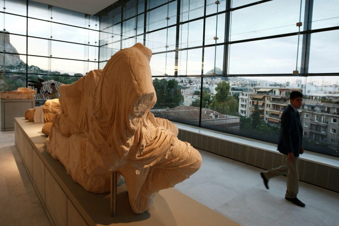 A recumbent, ochre-coloured statue on display inside the modern interior of the Acropolis Museum