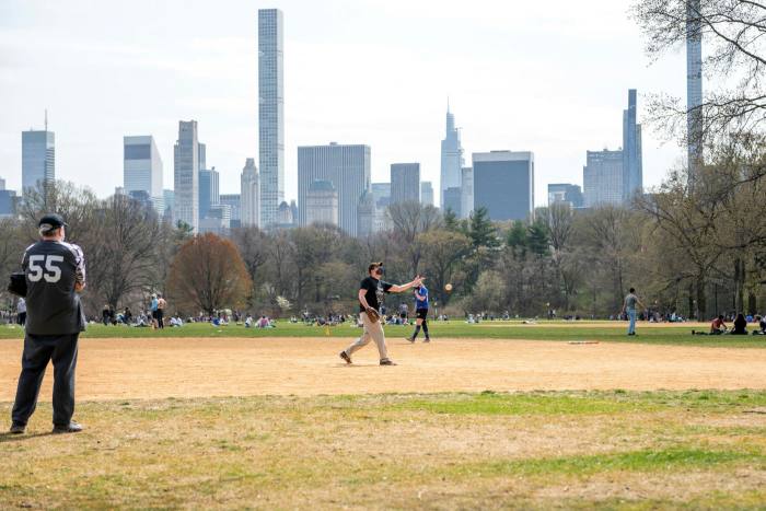 People wearing masks play softball on the large lawn in Central Park