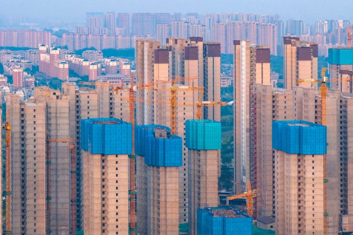 Endless rows of half-completed concrete tower blocks are attended by huge cranes 