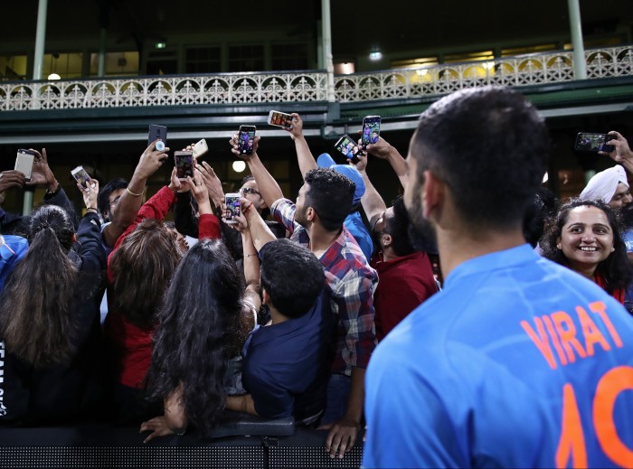 Cricket player Virat Kohli poses fans taking photos of themselves and the player with their phones