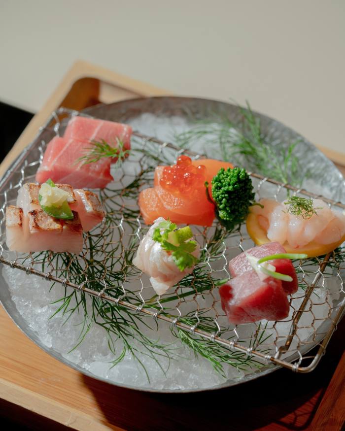 Six pieces of sashimi resting on a metal grid sitting on top of a an ice-filled metal dish at Hakata TonTon