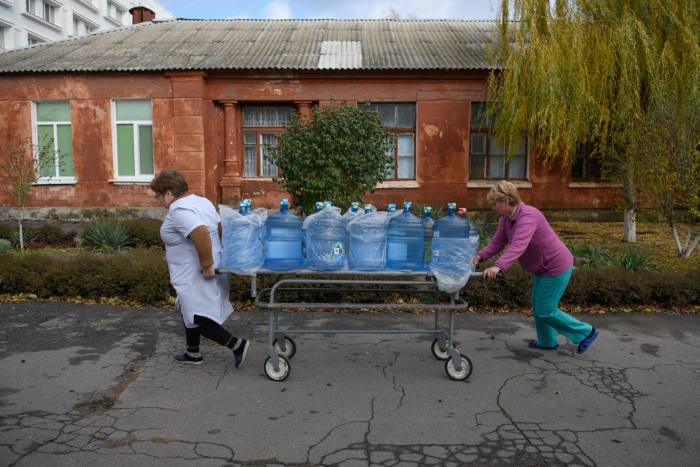 Two women manoeuvre a trolley, laden with water bottles, along a street