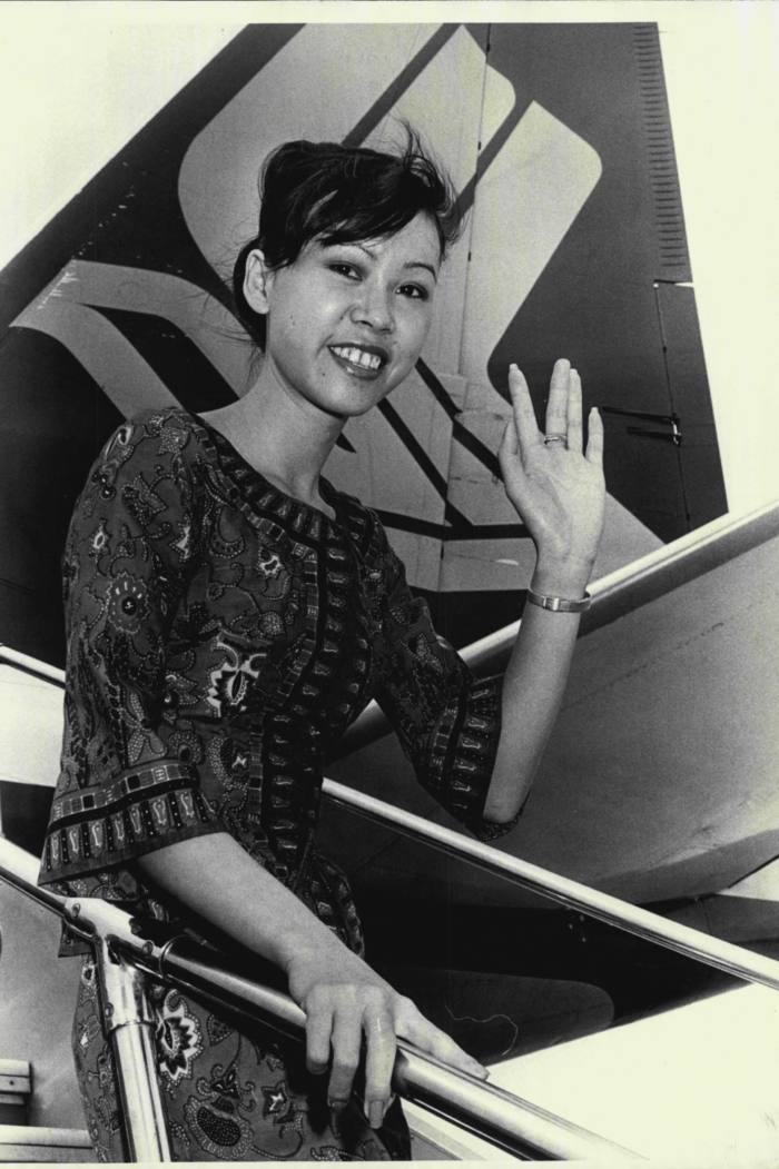 A smiling young woman waves from the steps of an aircraft