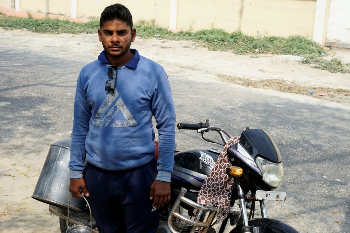 Ajit Yadav holds a milk can and stands in front of his motorbike  