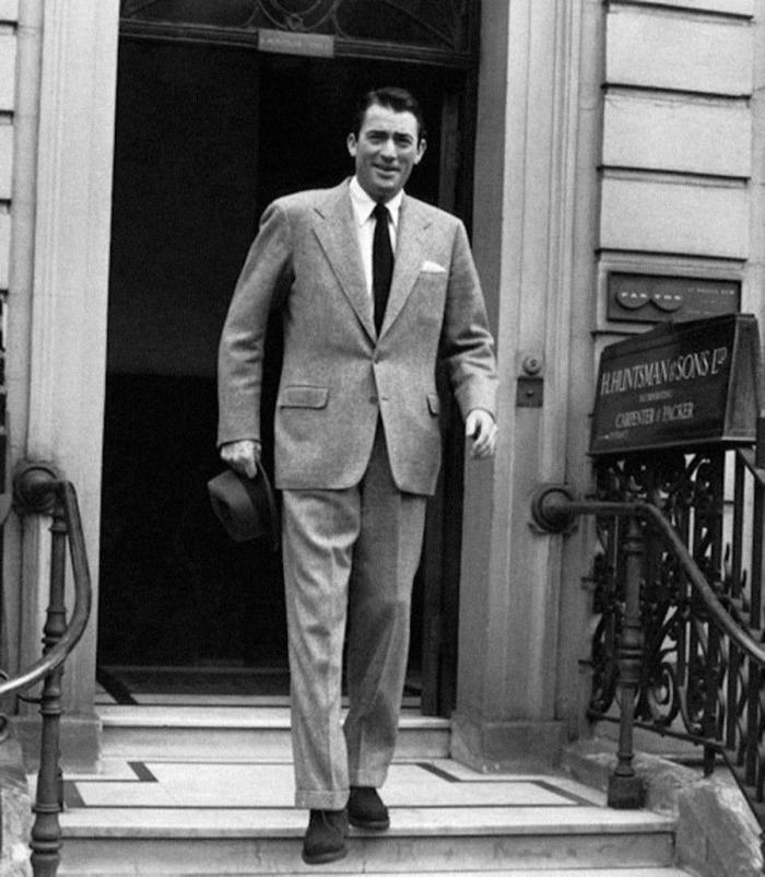 A black and white photograph of Gregory Peck standing at the top of the steps outside Huntsman in the mid 1950s