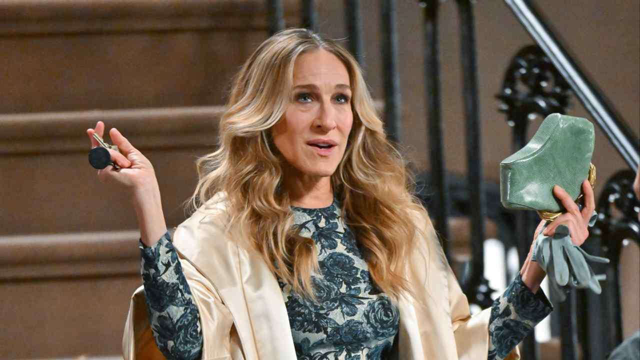 Sarah Jessica Parker stands at the bottom of a flight of stairs holding a small green bag in one hand and her keys in the other