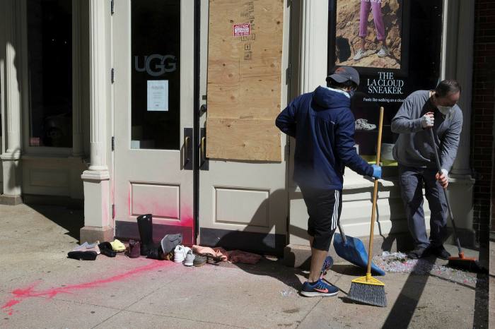 Cleaning crew board up windows and sweep away broken glass of an UGG store in Boston, Massachusetts, on Monday