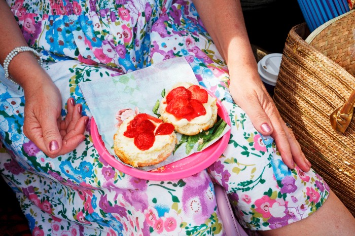 A plate of strawberries and cream on scones, on the lap of a woman wearing a purple and green floral dress