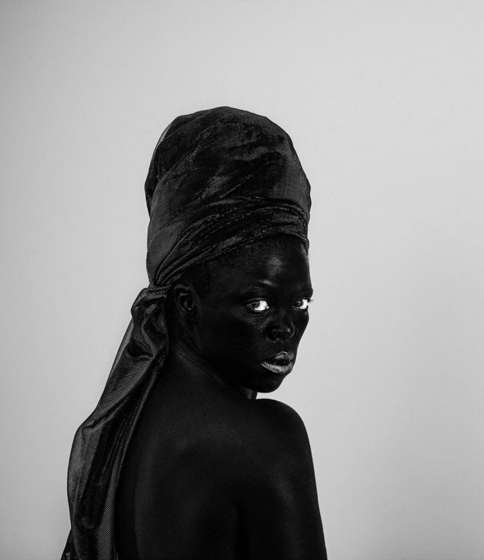 A black and white photograph shows a black woman wearing a turban, looking over her should