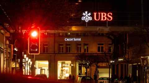Neonový nápis Credit Suisse vidět za nápisem UBS v noci v Curychu