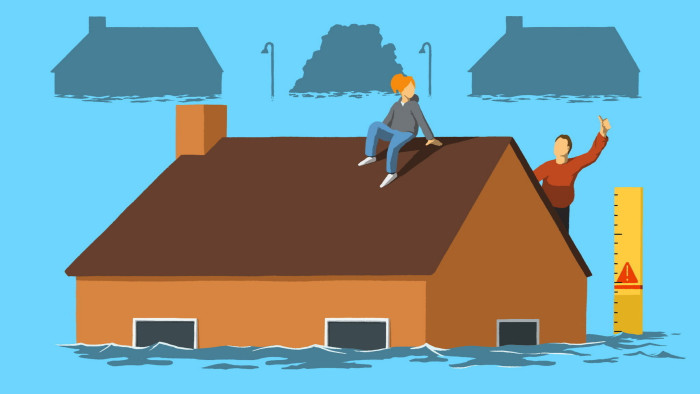 A man and woman sit on the roof of a partially submerged house with a depth gauge in the water beside the house
