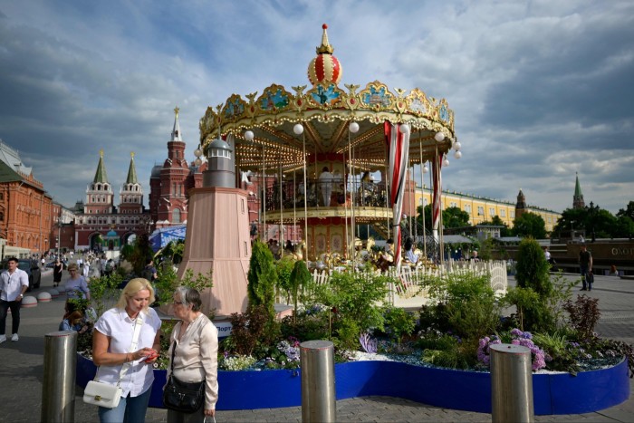 Women stand in front of a merry-go-round at Manezhnaya square near the Kremlin in Moscow
