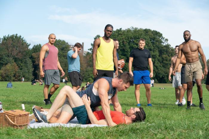 One man pins another to the ground in park while others look on