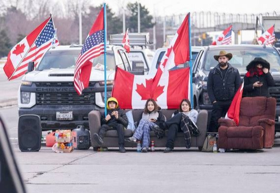 Protestors waving US and Canadian flags block the Ambassador Bridge with trucks, a sofa and an armchair
