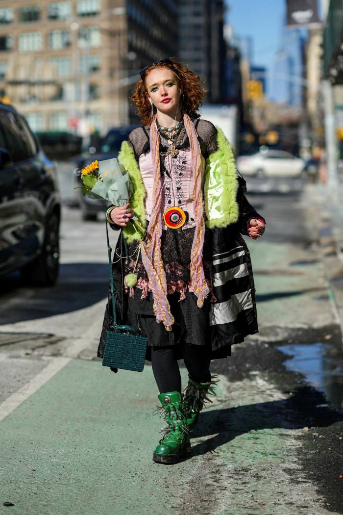 A guest wears a green fluffy jacket, a black long coat, a black pleated knees skirt, a dark green shiny leather crocodile print pattern handbag, green shiny leather ankle boots, outside Bibhu Mohapatra, during New York Fashion Week