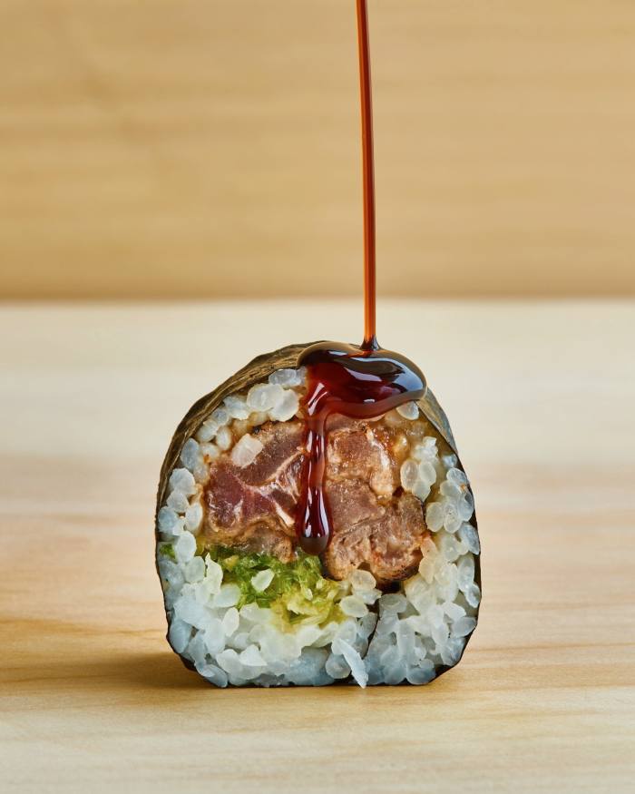 A roll of sushi with a dark sauce dribbling on top of it at Jōji