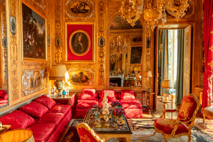An extremely grand sitting room with golden walls and red silk sofas