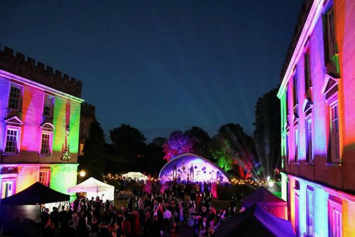 Oxford commemoration ball; partygoers are in a garden with multicoloured lights projected onto building walls