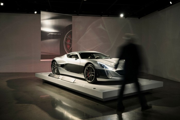 A man is silhouetted in front of a supercar in a showroom