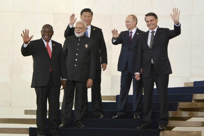 The leaders of South Africa, India, China, Russia and Brazil — all men in dark suits — wave to photographers from the steps to a building