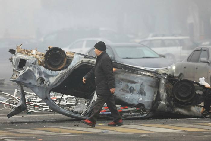 A man walks past an overturned car that was set on fire during protests in Almaty triggered by a fuel price increase