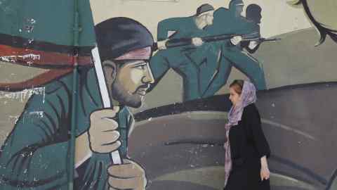 An Iranian woman walks past a mural Iranian revolutionary gaurd corps (IRGC) soldiers in Tehran