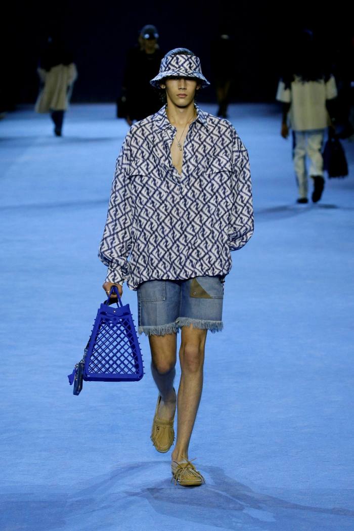 A male model wears denim shorts, patterned top and hat