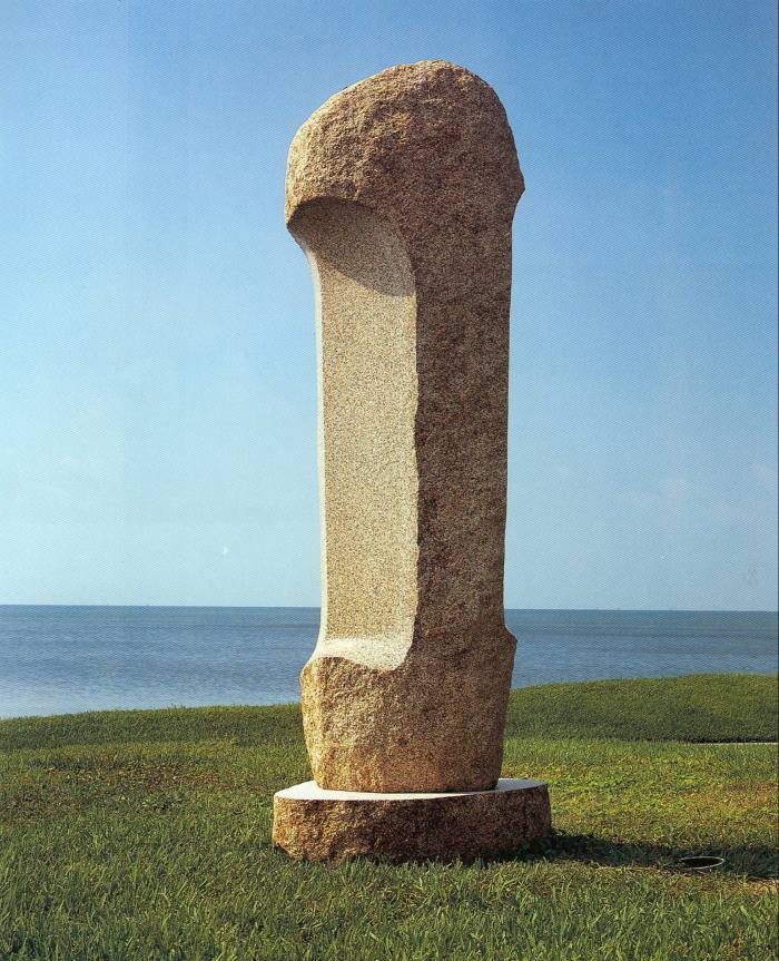 A granite obelisk in the shape of a bone stands upright on some grass