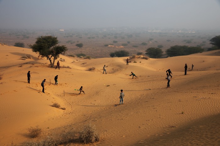 Locals spread out along desert dunes to play a game of cricket