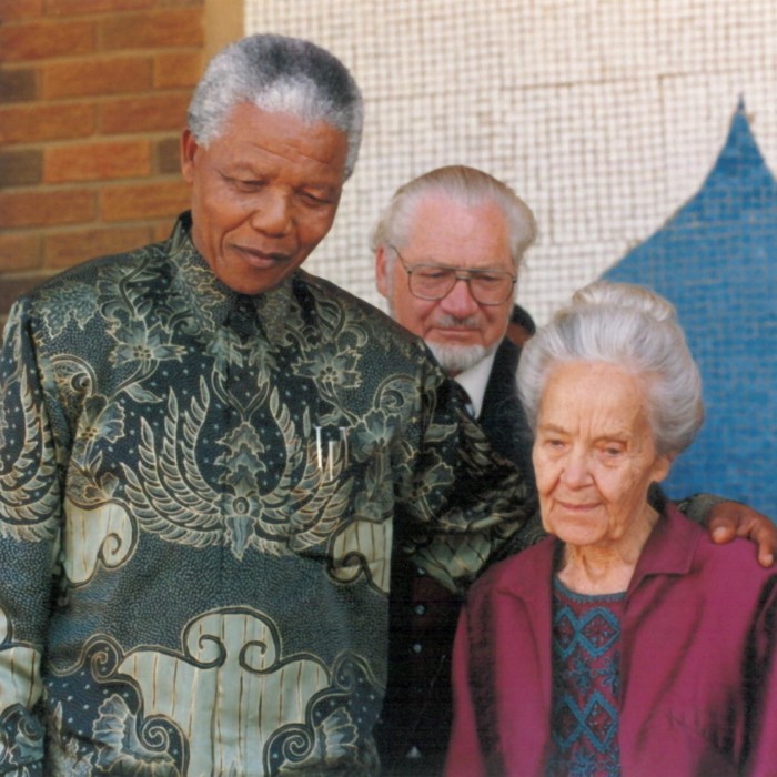 A colour photograph dated 1995 of Nelson Mandela in a dark green floral patterned shirt, his hand on the shoulder of a small elderly lady