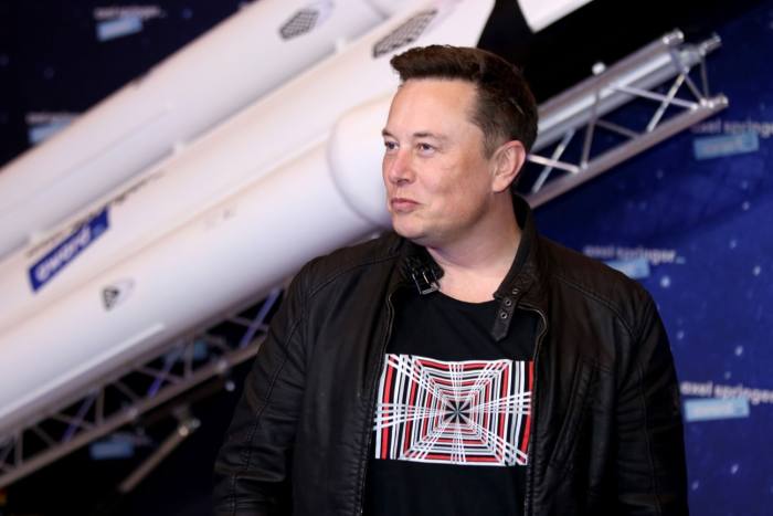 Elon Musk stands in front of a model of a rocket